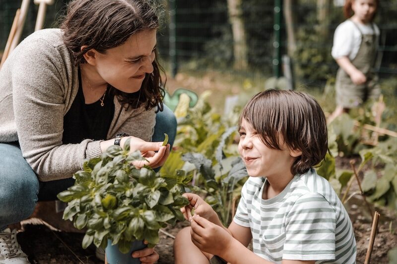 Erzieherin und Kind ernten lachend Gemüse im Kindergarten-Garten.