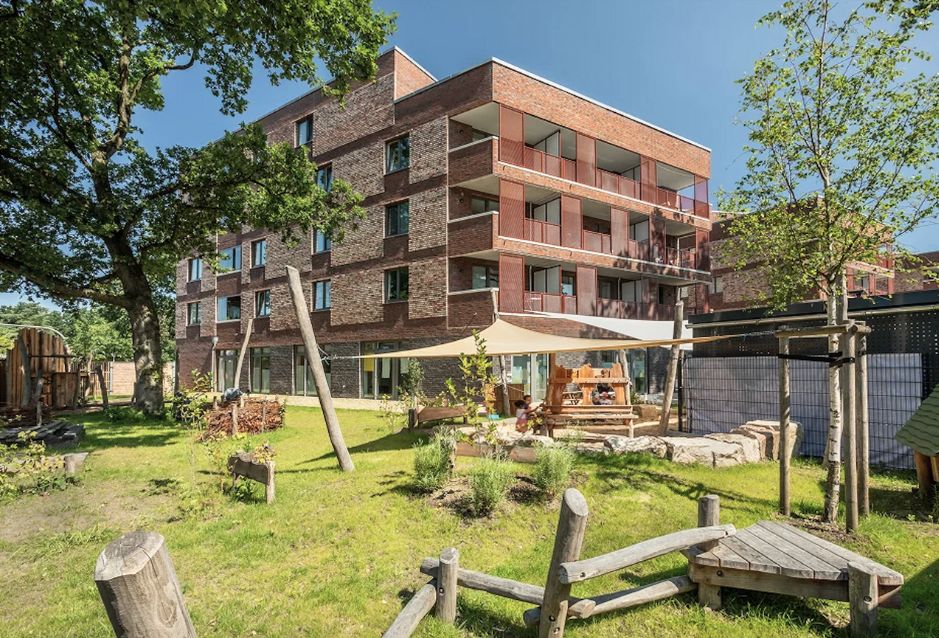 Modernes Backsteingebäude mit grünem Außenspielbereich und Sonnensegel.